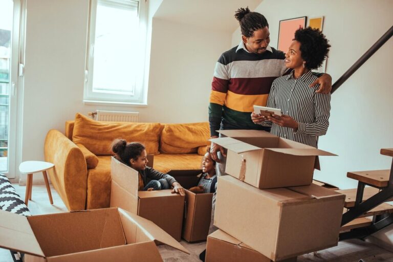 Familia afrodescendiente feliz en una sala de estar con un sillón amarillo y cajas de cartón, mudanza Bodega Guadalajara