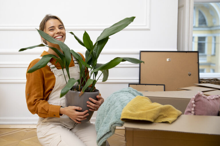 Mujer feliz cargando una maceta con una planta y de fondo cajas de cartón apiladas para mudanza Bodega Guadalajara