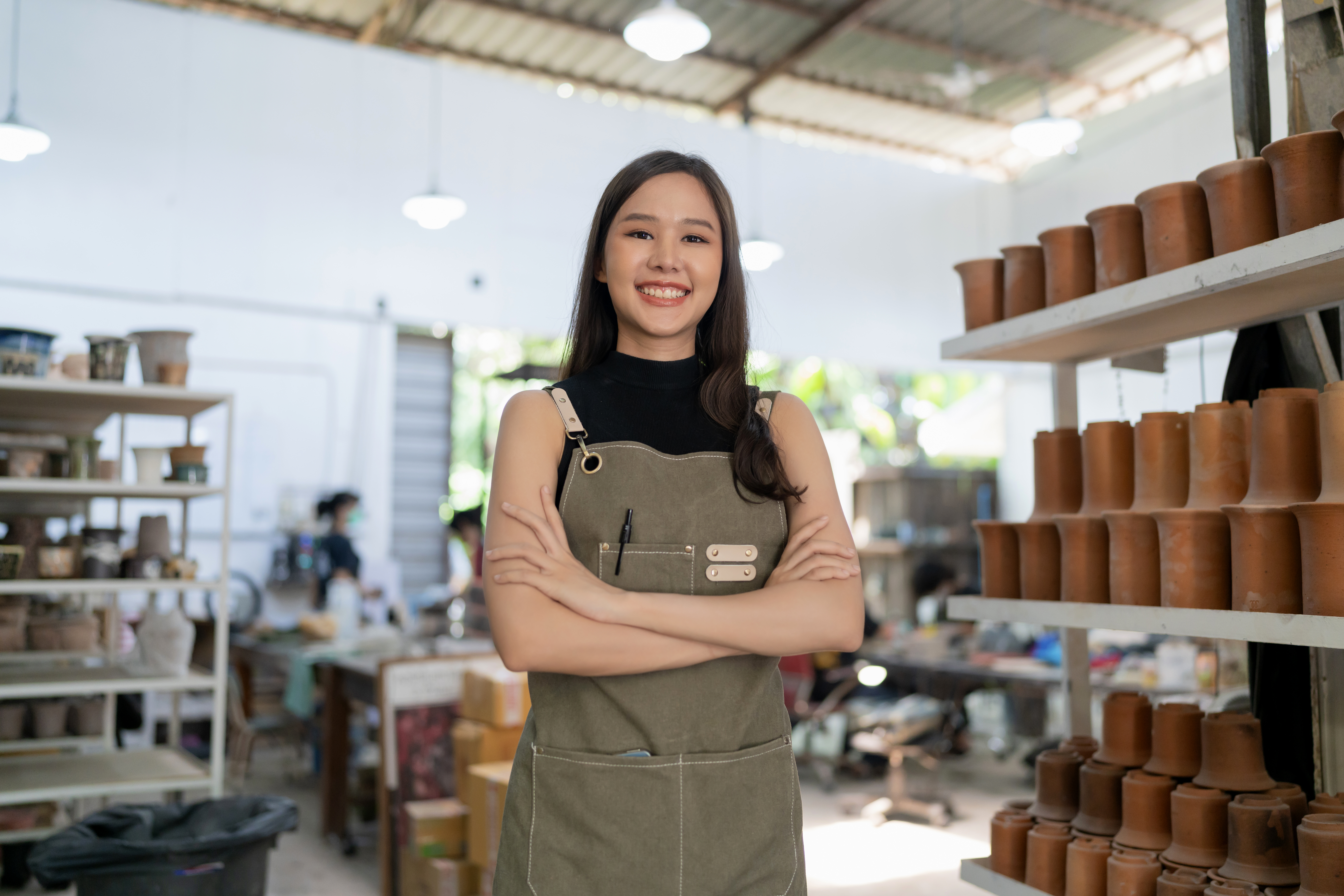 Asia female ceramist with apron hand confident chest in her workshop clay sculpture studio with positive smiling warm welcome ready to start new factory ceramic workshop with new collection of work