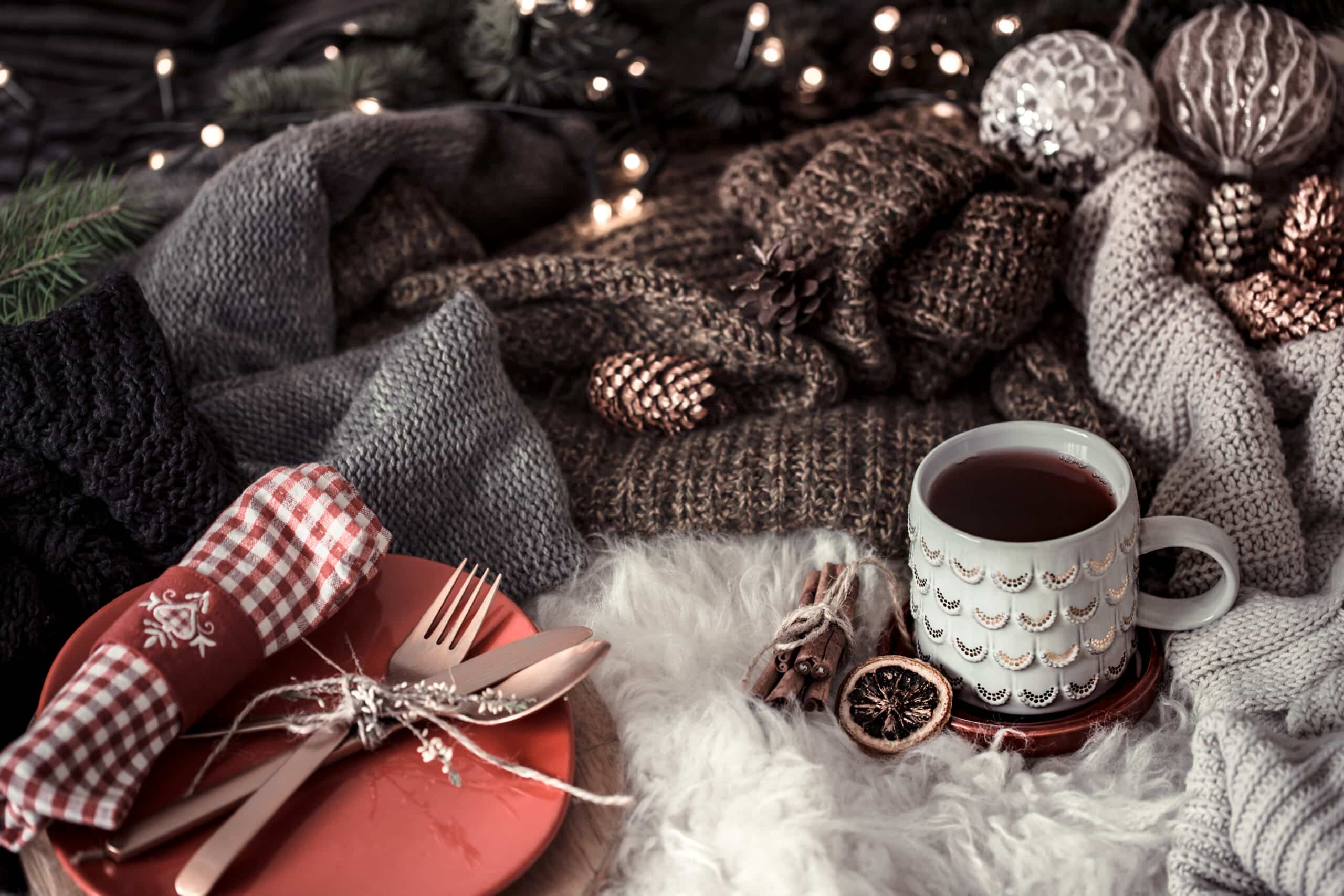 Cozy winter morning with cup of tea in bed. Steaming cup of hot coffee, tea standing near window. Christmas concept. Pillows, pine cones, gypsophila and fir tree branch on wool plaid.